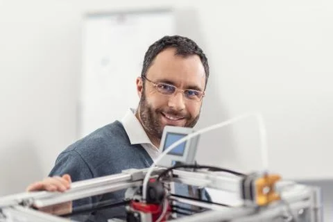 Joyful engineer in eyeglasses posing near 3D printer Stock Photos