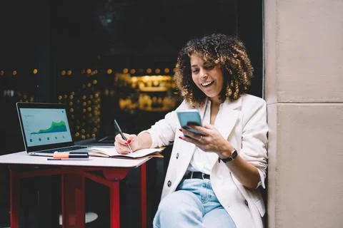 Joyful female using mobile application for online messaging in sidewalk cafe Stock Photos