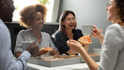 Joyful friendly multicultural team having fun eating pizza together Stock Photos