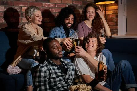 Joyful friends sitting at home and watching football game on television. Their Stock Photos
