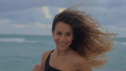 Joyful girl is jogging in cloudy day on shore of ocean, correcting her hair Video stock 96160271