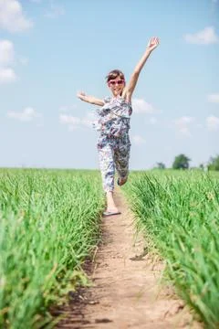 Joyful girl jumping high while walking through field Stock Photos