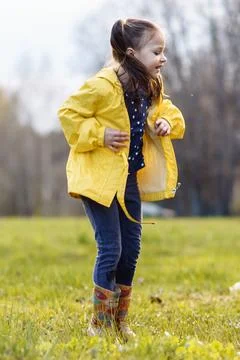 Joyful girl jumping up while standing in puddle on lawn, looking down with .. Stock Photos