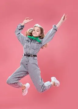 Joyful girl teenager in denim overalls jumping on a pink background. Happines Stock Photos