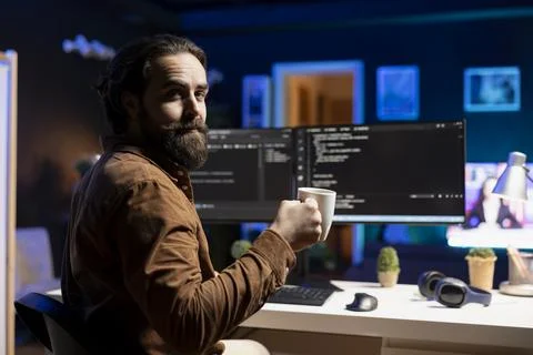 Joyful IT worker holding coffee mug and debugging code Foto stock