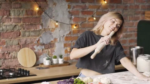 Joyful lady dances at kitchen table singing into rolling pin Stock Footage 149844772