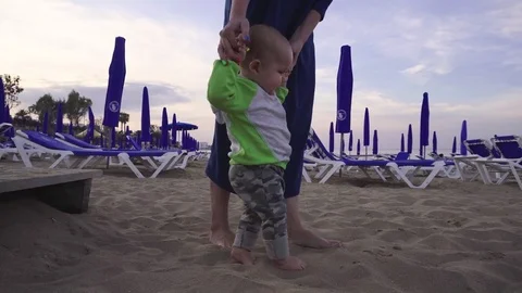 Joyful little boy makes first steps on a sandy beach holding mother's hands 動画素材 76856114