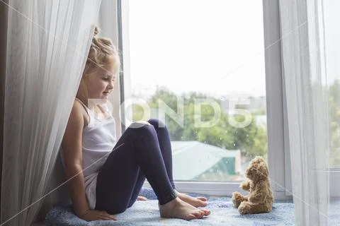 Joyful little girl sitting on the windowsill Stock Photos