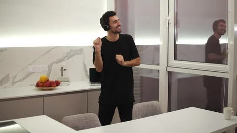 Joyful man in black clothes is dancing in kitchen listening to music with Stock Footage 123935292