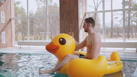 Joyful man is calling by video in mobile phone from modern swimming pool, riding Video stock 186613843