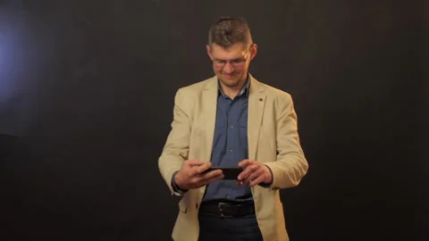 Joyful man in glasses types on black smartphone and hides Stock Footage 135390923