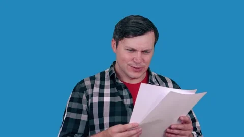 Joyful man looks at paper with documents, reading document, on blue background. Stock Footage 148374271