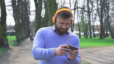 Joyful man in park playing game on smartphone app, portrait steadicam shot 库存影片 74233170