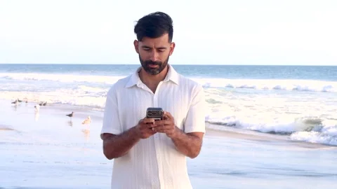 Joyful man standing on the beach reading good news on his smartphone and ce.. Stockbeeldmateriaal 337854666