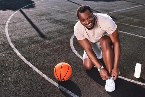 Joyful man tying his shoelaces on a basketball court Stock Photos