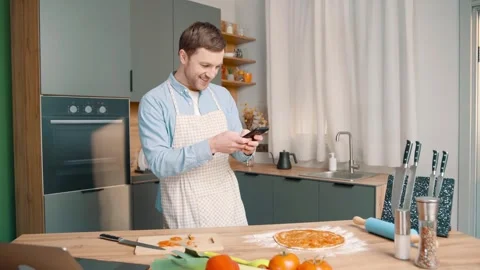 Joyful man wearing apron prepares pizza in modern kitchen Stock Footage 248523624