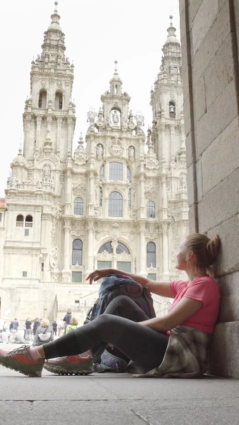 Joyful middle-aged backpacker pilgrim woman sitting on Obradoiro square in Santi Stock Footage 311087023