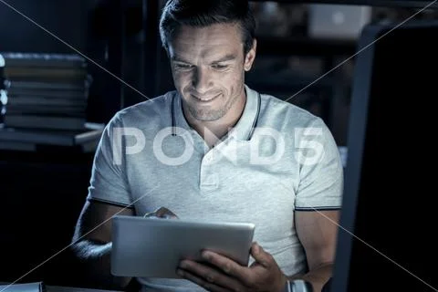 Joyful millennial man smiling while working on touchpad Stock Photos