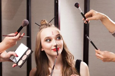 Joyful model surrounded by hands holding brushes Stock Photos