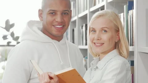 Joyful multiethnic couple beaming at the camera while sharing a book Stock Footage 311951765