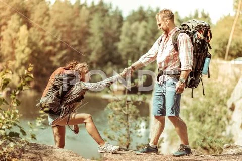 Joyful nice man helping his girlfriend to climb Stock Photos