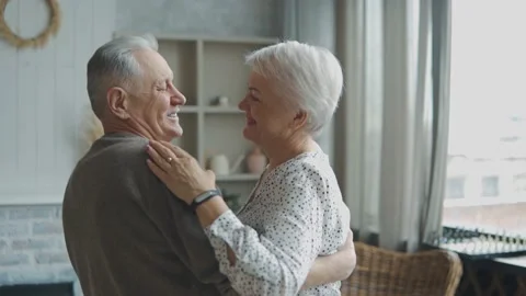 Joyful old couple dancing looking at each other in the living room Stockbeeldmateriaal 171990920