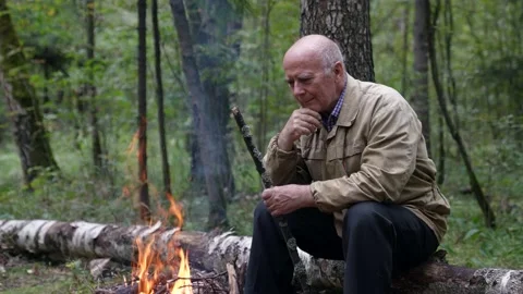 Joyful old man is resting in forest, looking at burning fire, rest in nature Video stock 166803791