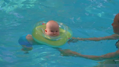 Joyful one year old boy swimming in pool with mother, wearing inflatable neck Stock Footage 336342728