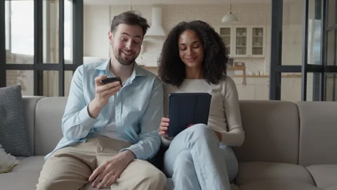 Joyful Pair Relaxing Sofa, Man Holding Remote, Woman Engaged With Tablet Screen Stock Footage 303759849