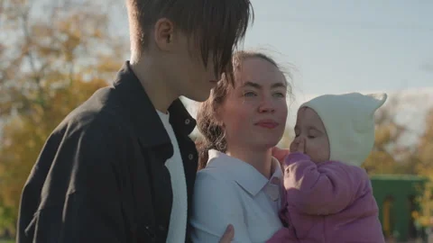 Joyful parents interact with child under sunlit fall trees. Relaxed family Stock Footage 334622376
