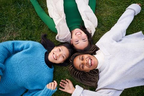 Joyful portrait of three best friends lying on grass having good time laughing Stock Photos