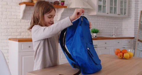 Joyful school kid packing backpack in kitchen, feeling excited and ready for Stock Footage 317070867