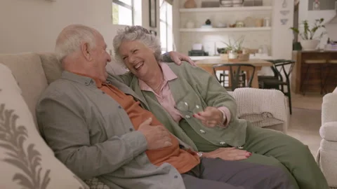 Joyful senior couple sitting on a couch having a conversation at home Stock Footage 334953776