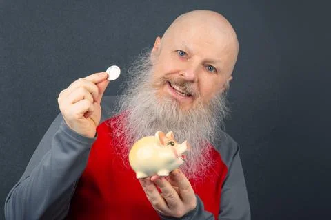 Joyful senior man with a white beard saving money in a piggy bank, represen.. Stock Photos