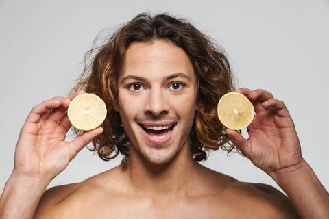 Joyful shirtless guy smiling while posing with lemon Foto stock