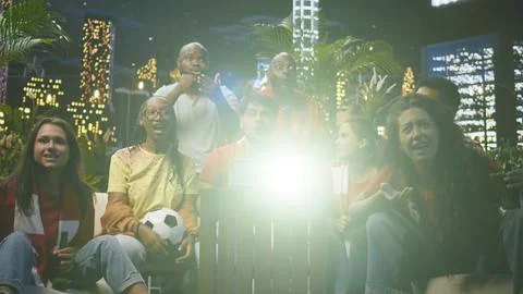Joyful soccer supporters using projector to watch match, cheering together Stock Photos