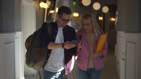 Joyful student couple talking and using cellphone while walking in college Stock Footage 139054166