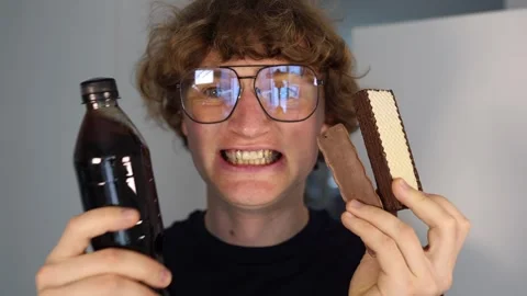 Joyful sugar rush as young man excitedly holds chocolate wafers and soda with wi Stock Footage 312201781