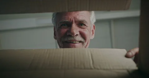 Joyful surprised gray-haired senior man pensioner opening cardboard box with 库存影片 139529701