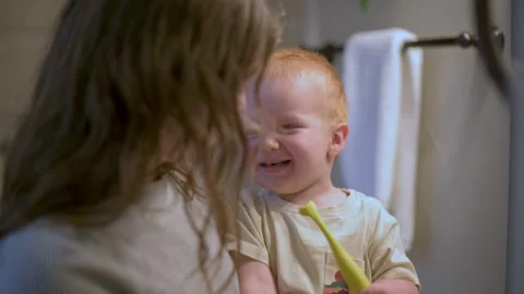 Joyful toddler laughs while brushing teeth, with mother nearby in bathroom Vídeo Stock 289678438