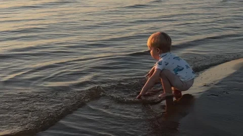 Joyful toddler splashes water while playing in shallow river at sunset Stock Footage 314308613