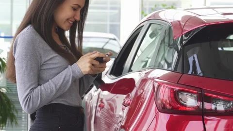 Joyful woman using smartphone while standing next to a shiny red car Stock Footage 311535540