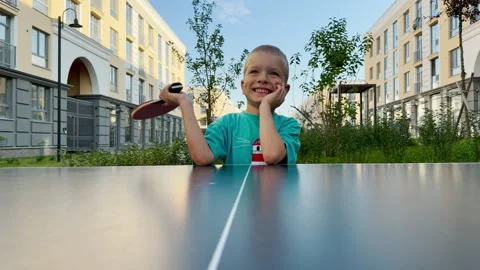 A joyful young boy rests his head and smiles while holding a ping pong paddle. Video stock 344990227