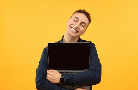 Joyful young guy hugging open laptop, yellow background 写真素材