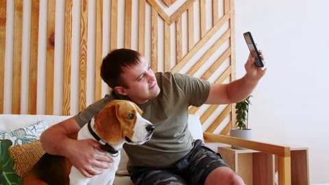 A joyful young man sitting at table and hugging her Dog Beagle while making Stock Footage 162817385