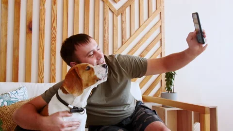 A joyful young man sitting at table and taking selfie with pet using phone. Mans Stock-Footage 162949289