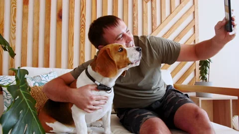 A joyful young man sitting at table and hugging her Dog Beagle while making Stock Footage 163207955