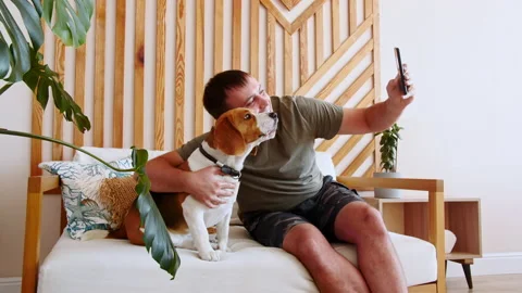 A joyful young man sitting at table and taking selfie with pet using phone. Mans Stock Footage 163448111