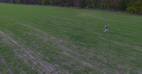 Joyful young man wearing a jacket running on the field - Aerial view Stock Footage 62793440