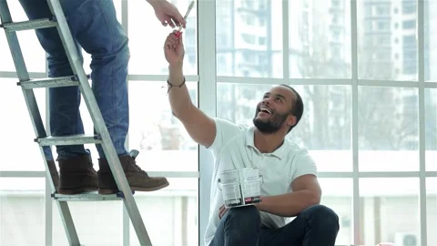 Joyful young painter man sitting on a window sill, reaching for a paintbrush Stock Footage 311808385